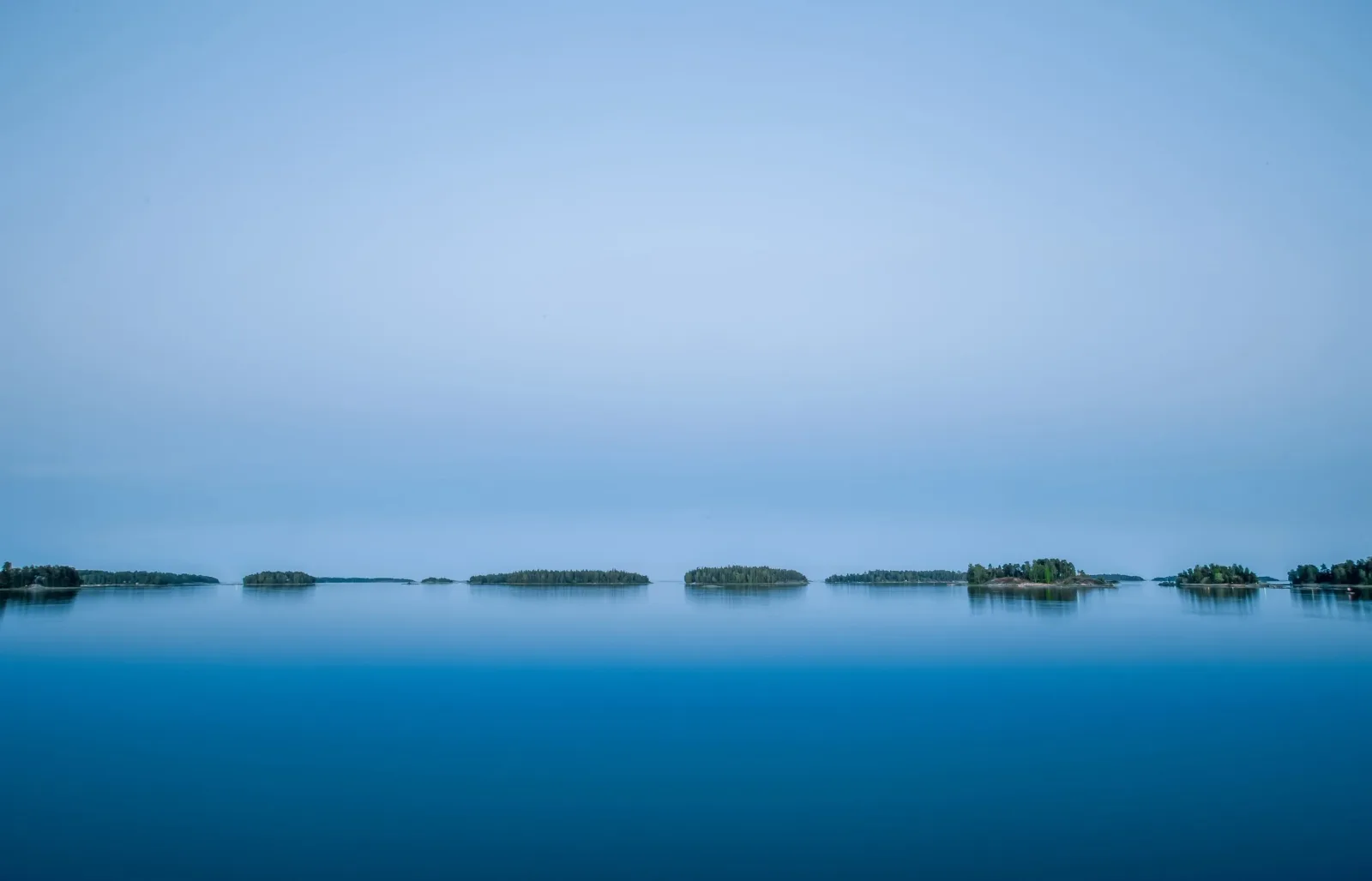 Stilla blått vatten med skogklädda holmar vid horisonten