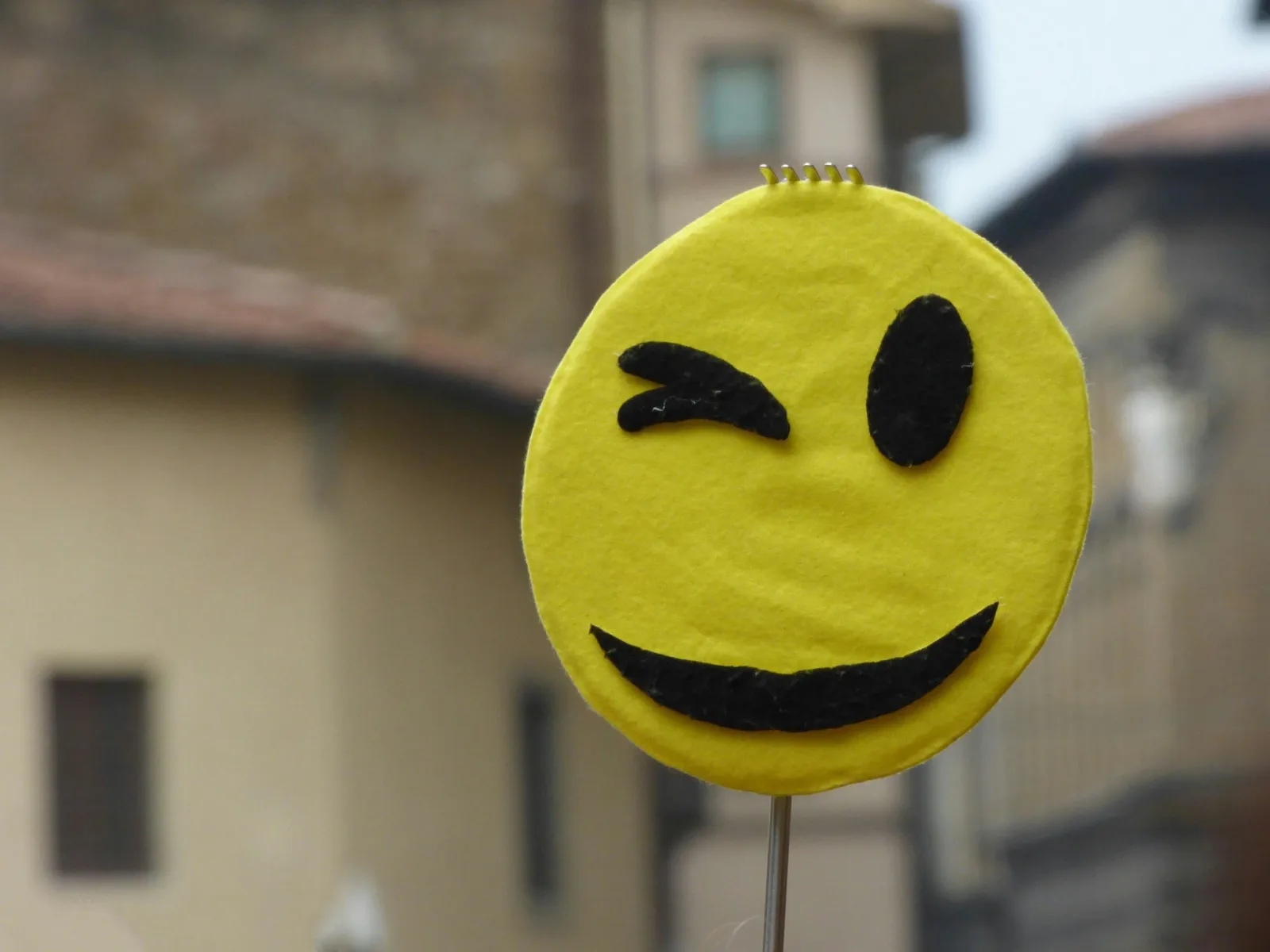 Ett gult smileyansikte av filt på en pinne, blinkande och leende