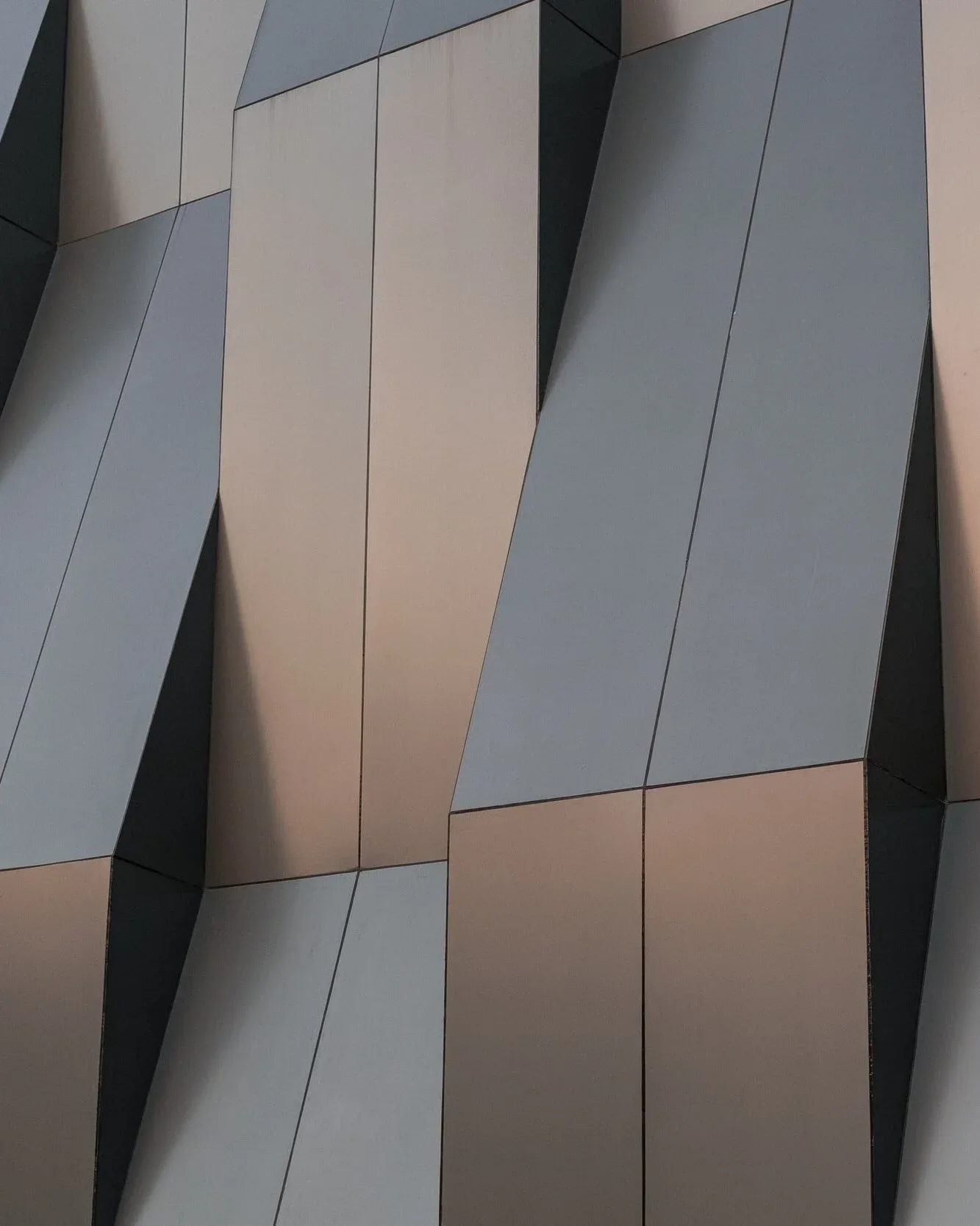 Abstrakt fasad med vikta geometriska paneler i grått och koppar