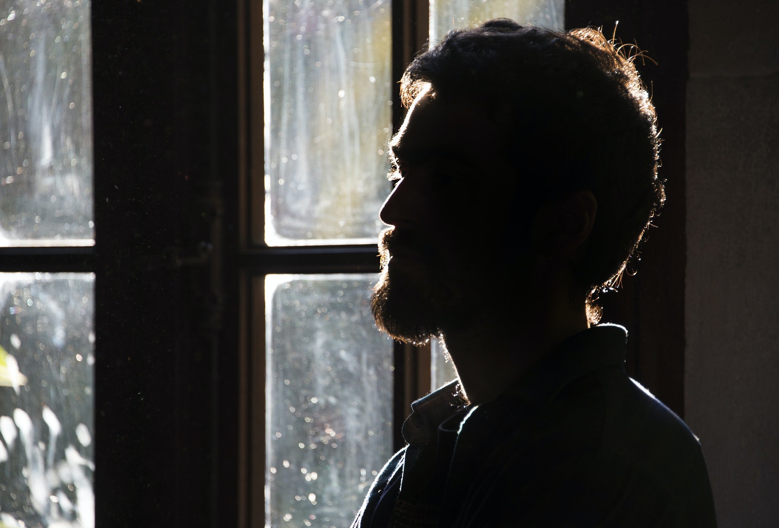 Man sedd i profil, bakåtbelyst av ett fönster inomhus, ansiktet i skugga