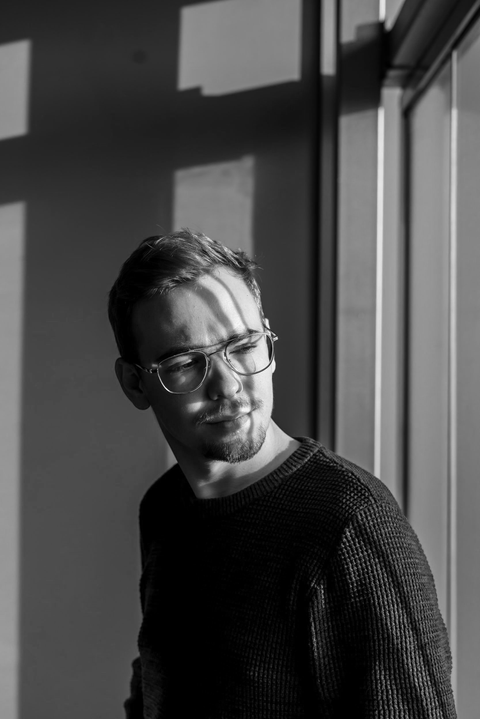 Man i rödbrun tröja och glasögon, sedd i profil vid ett fönster